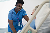 caring female nurse talking with patient in hospital bed