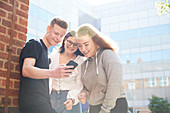 Teenage friends using smart phone outside school