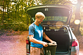 Smiling man preparing for hike at back of sunny car