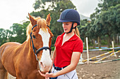 Teenage girl in equestrian helmet with horse in paddock