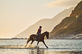 Young woman galloping on horseback in tranquil ocean surf