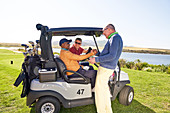 Male golfer friends talking at golf cart