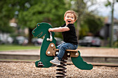 Toddler girl riding dinosaur toy at playground