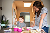 Mother and cute toddler daughter baking at kitchen table