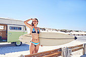 Young female surfer with surfboard on sunny summer beach