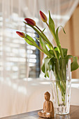 Tulip bouquet in vase and wooden Buddha statuette