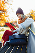 Woman using digital tablet on autumn park bench
