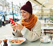 Woman with smart phone eating lunch at cafe