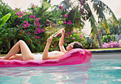 Woman relaxing, reading book on pool raft in swimming pool