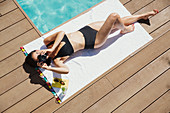 Woman sunbathing, using digital camera at poolside