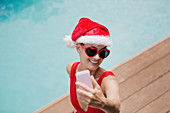 Woman in Santa hat taking selfie at poolside