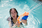Playful woman using squirt gun in summer swimming pool