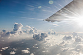 Airplane wing moving through tranquil, sunny, cloudy sky