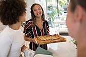 Woman serving homemade pizza to friends in kitchen