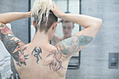 Woman with tattooed back at bathroom mirror