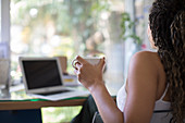 Woman drinking tea at laptop in home office