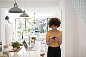 Young female freelancer using smart phone in kitchen