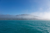 Fog breaking over mountains and turquoise blue ocean
