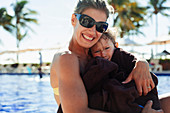 Portrait mother holding son wrapped in towel at poolside