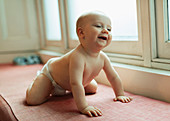 Cute baby girl in diaper laughing on window seat