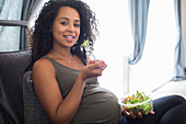 Portrait smiling pregnant woman eating salad on sofa