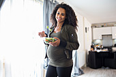 Portrait happy pregnant woman eating salad at window