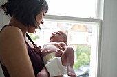 Mother holding cute newborn baby boy at window