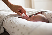 Mother holding hands with newborn baby son in bassinet