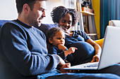 Young pregnant family using laptop on sofa