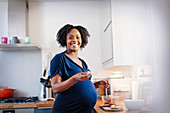 Portrait happy pregnant woman eating in kitchen