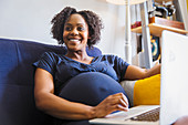 Happy pregnant woman using laptop on sofa