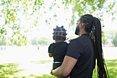 Father with long braids carrying son in park