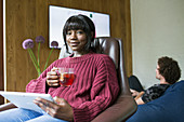 Woman drinking tea and using digital tablet in living room