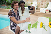 Happy couple taking selfie with camera phone at poolside