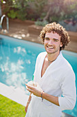 Portrait man in bathrobe drinking from coconut at poolside