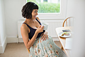 Happy pregnant woman drinking tea at laptop