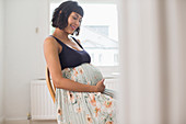 Happy pregnant woman in floral dress holding stomach