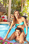 Young couple playing chicken in sunny summer swimming pool
