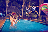 Young men friends jumping into swimming pool at night