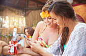 Young women friends drinking and texting at summer poolside