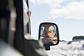 Young woman wearing sunglasses in side-view mirror of car