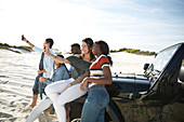 Young friends phones taking selfie at jeep on sunny beach