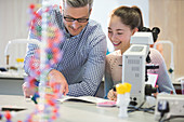 Male teacher helping girl student at microscope in classroom