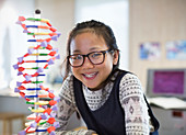 Confident girl student next to DNA model in classroom