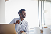 Smiling man drinking coffee and working at laptop at home