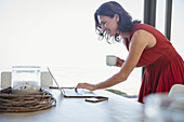 Brunette woman drinking coffee and using laptop