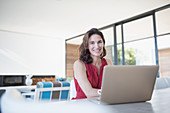 Portrait smiling brunette woman working at laptop in kitchen