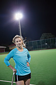 Serious young female field hockey player on field at night