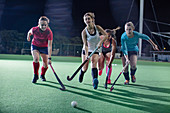 Female hockey players running for the ball