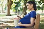 Pregnant woman texting with cell phone on park bench